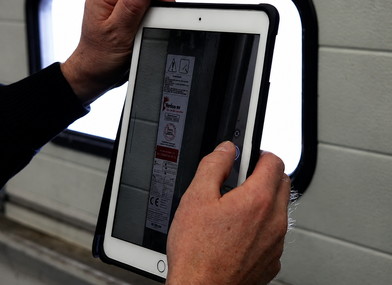 Monteur maakt een foto van een installatie met een tablet voor digitale inspectie en werkbonregistratie.