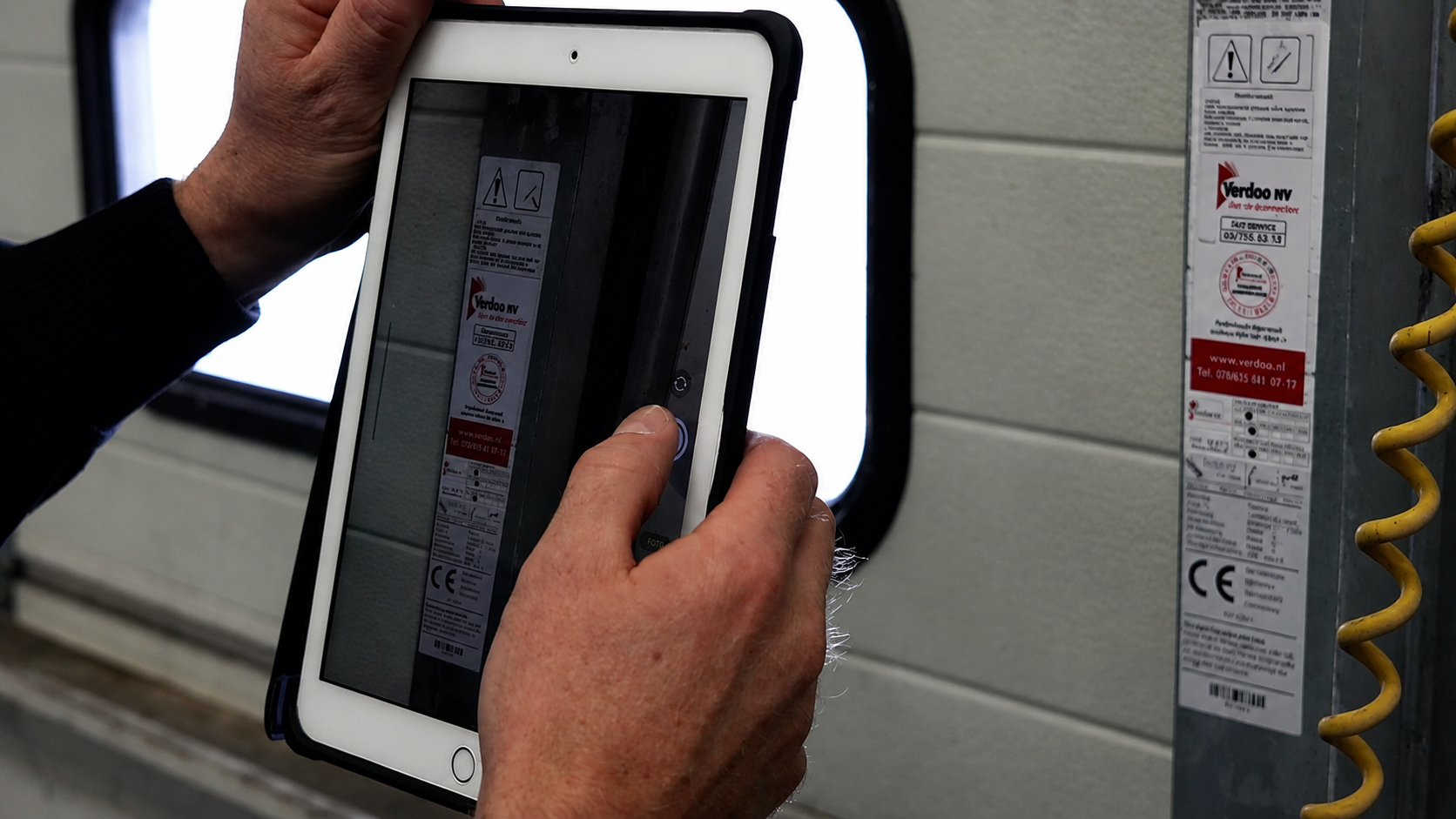 Monteur maakt een foto van een installatie met een tablet voor digitale inspectie en werkbonregistratie.