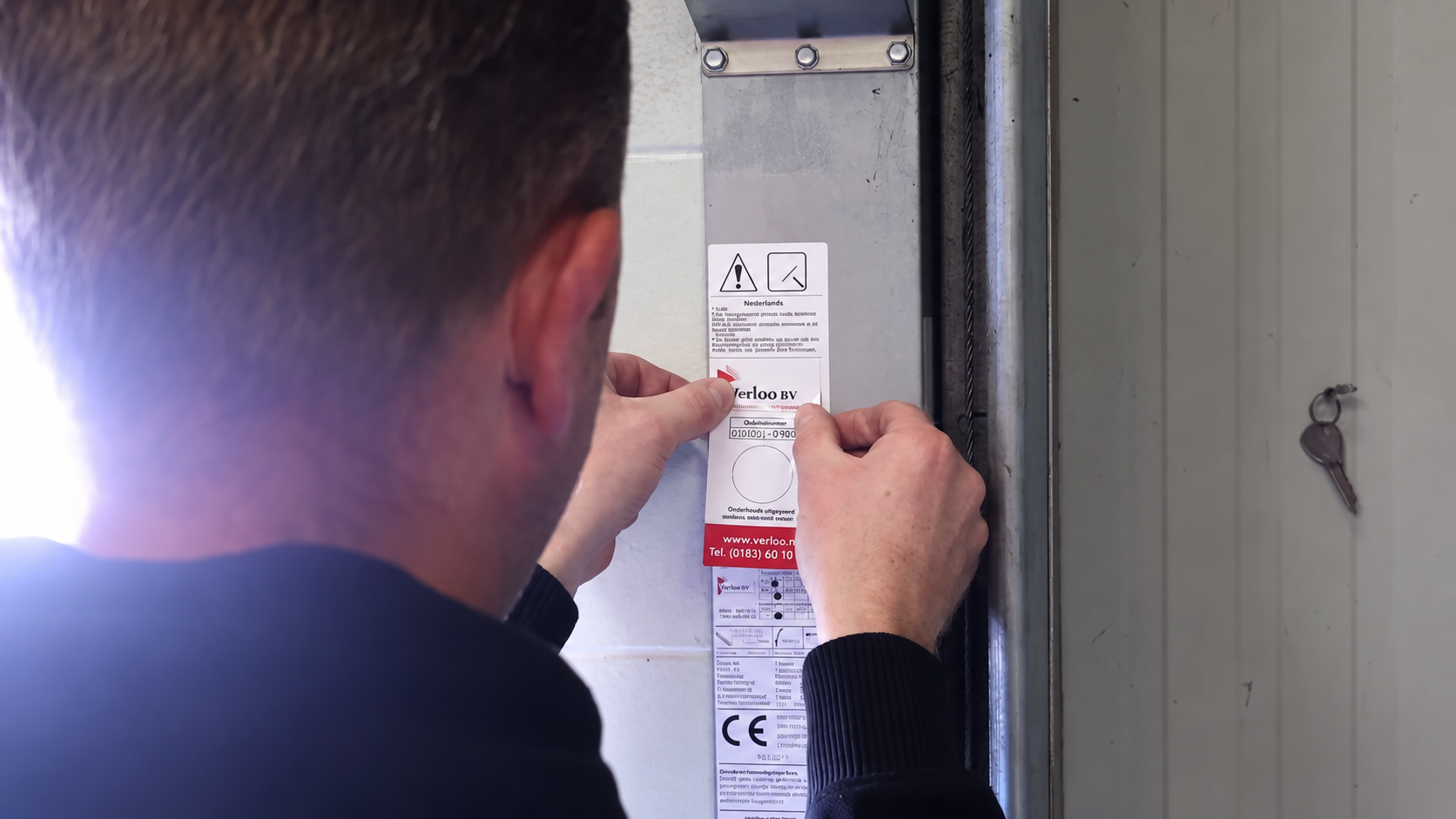 Monteur plaatst een onderhoudssticker op een installatie na uitgevoerd onderhoud.