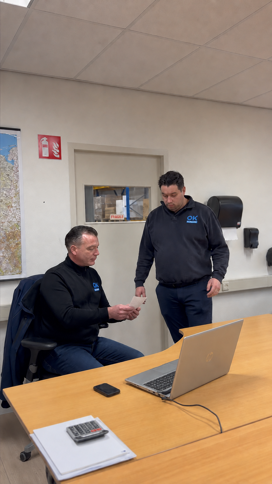 Twee servicemonteurs bespreken samen een papieren werkbon op kantoor.