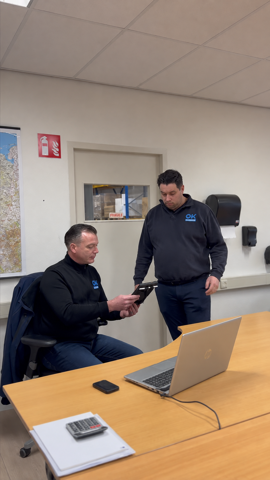 Twee servicemonteurs bekijken samen informatie op een tablet op kantoor.