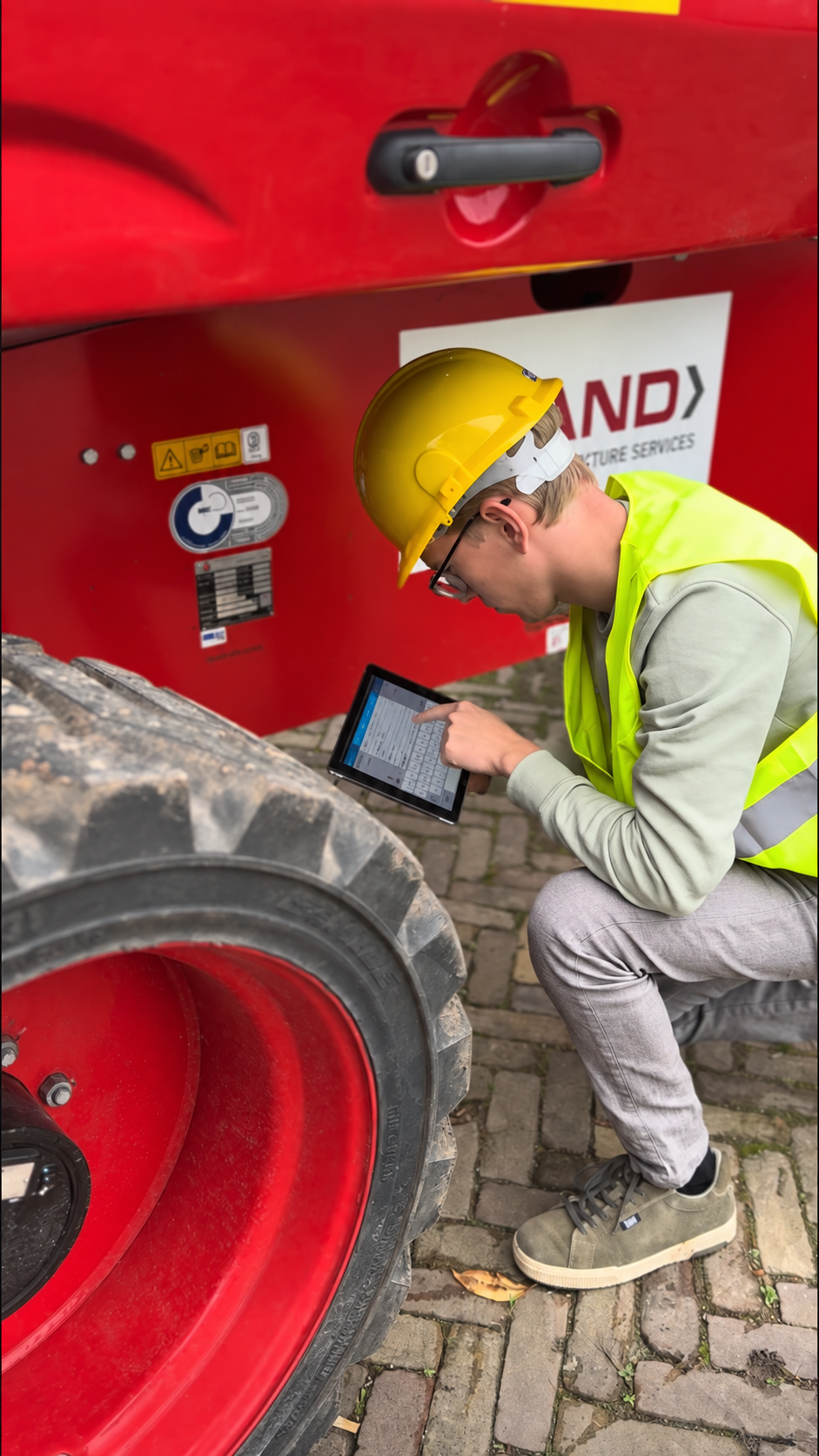 Monteur met veiligheidshelm en veiligheidshesje gebruikt een tablet bij een machine.