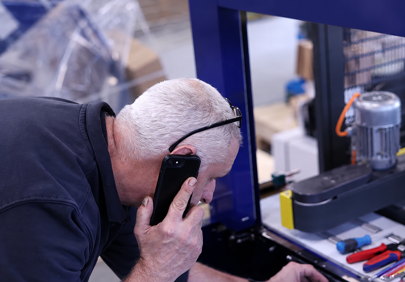 Monteur aan het werk bij een industriële machine terwijl hij telefoneert.