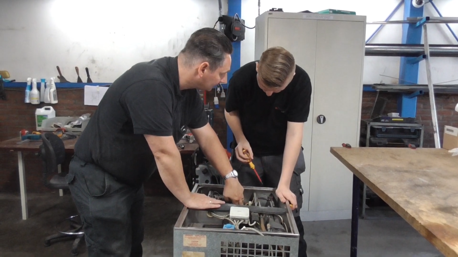 Twee monteurs voeren samen onderhoud uit aan een technische installatie in een werkplaats.