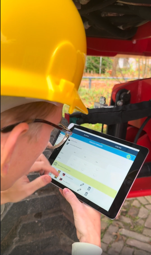 Monteur met veiligheidshelm gebruikt een tablet tijdens onderhoud aan een machine.
